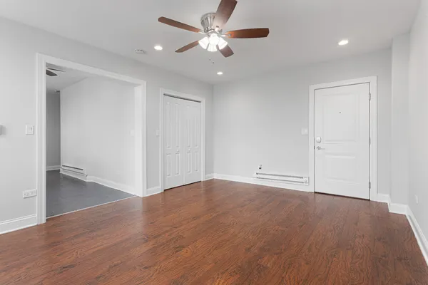 a view of an empty room with wooden floor and a ceiling fan