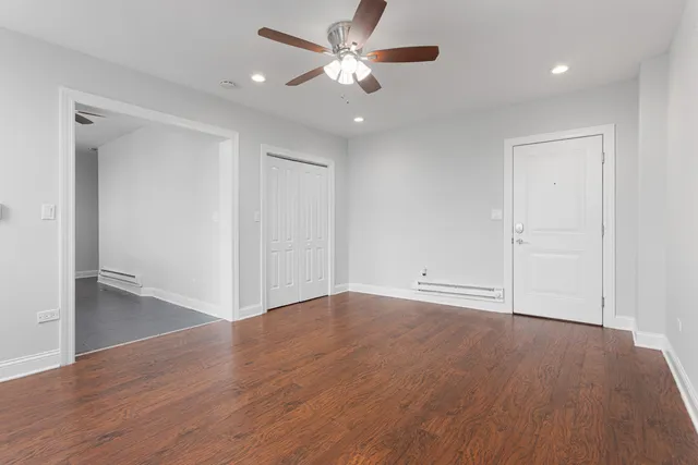 a view of an empty room with wooden floor and a ceiling fan