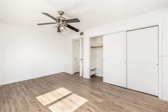 an empty room with wooden floor a ceiling fan and windows