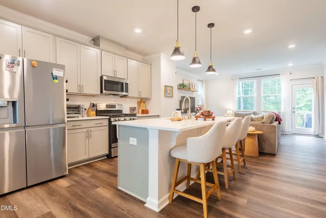 a kitchen with stainless steel appliances a stove a sink a refrigerator a dining table and chairs with wooden floor