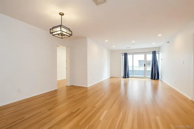 a view of an empty room with wooden floor and chandelier