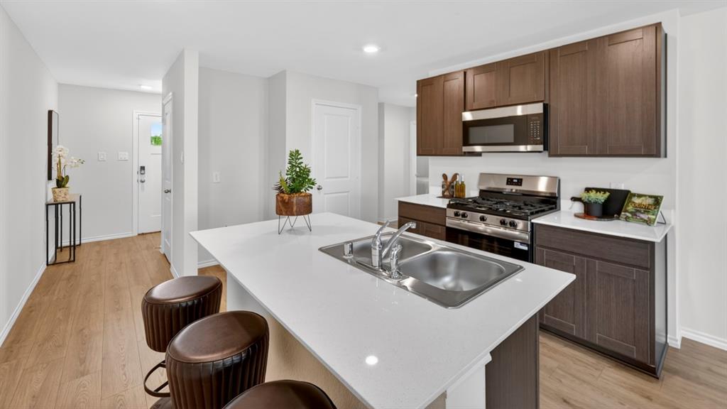3514 Spring Time Street Terrell, TX 75126 - Photo 6 of 26 Modern kitchen featuring a large island with an undermount double-basin sink, white countertops, dark wood-finish cabinetry, stainless steel appliances, and wood-finish flooring
