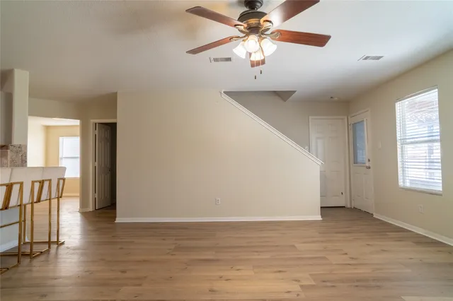 an empty room with wooden floor chandelier fan and windows