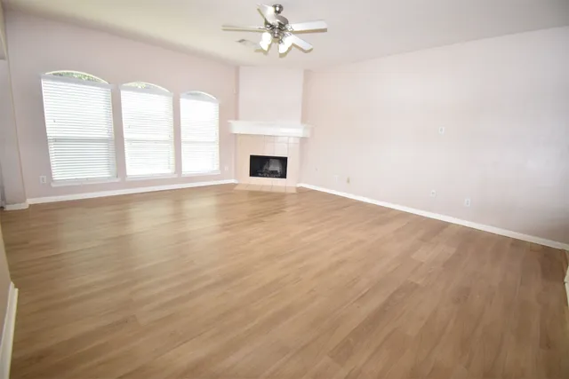 an empty room with wooden floor chandelier fan and windows