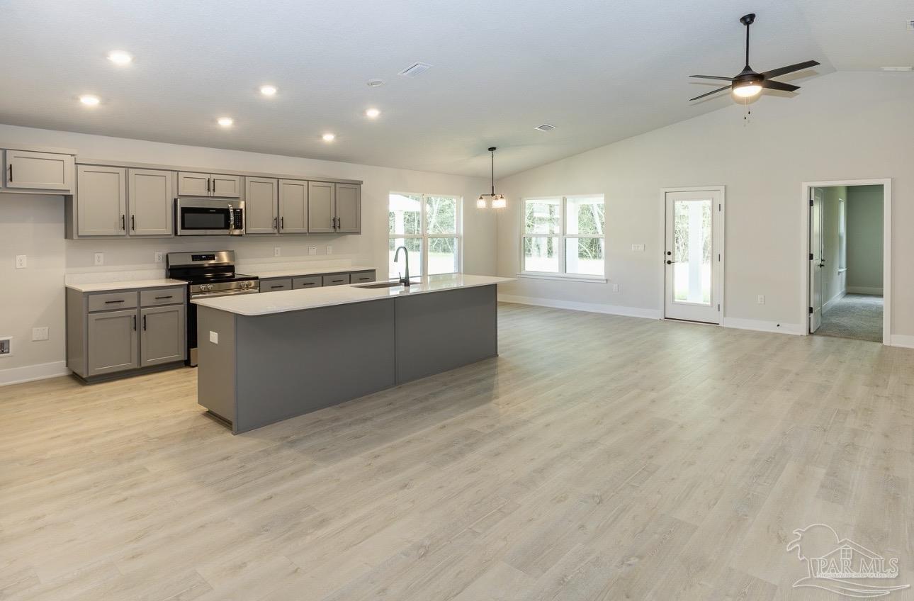 7657 Small Pnes Street Milton, FL 32583 - Photo 9 of 26 a large kitchen with stainless steel appliances granite countertop a stove top oven a sink dishwasher and a refrigerator with wooden floor