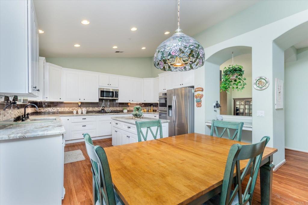 16350 Open View Road Ramona, CA 92065 - Photo 11 of 45 a kitchen with stainless steel appliances granite countertop a sink dishwasher a stove a refrigerator a dining table and chairs with wooden floor