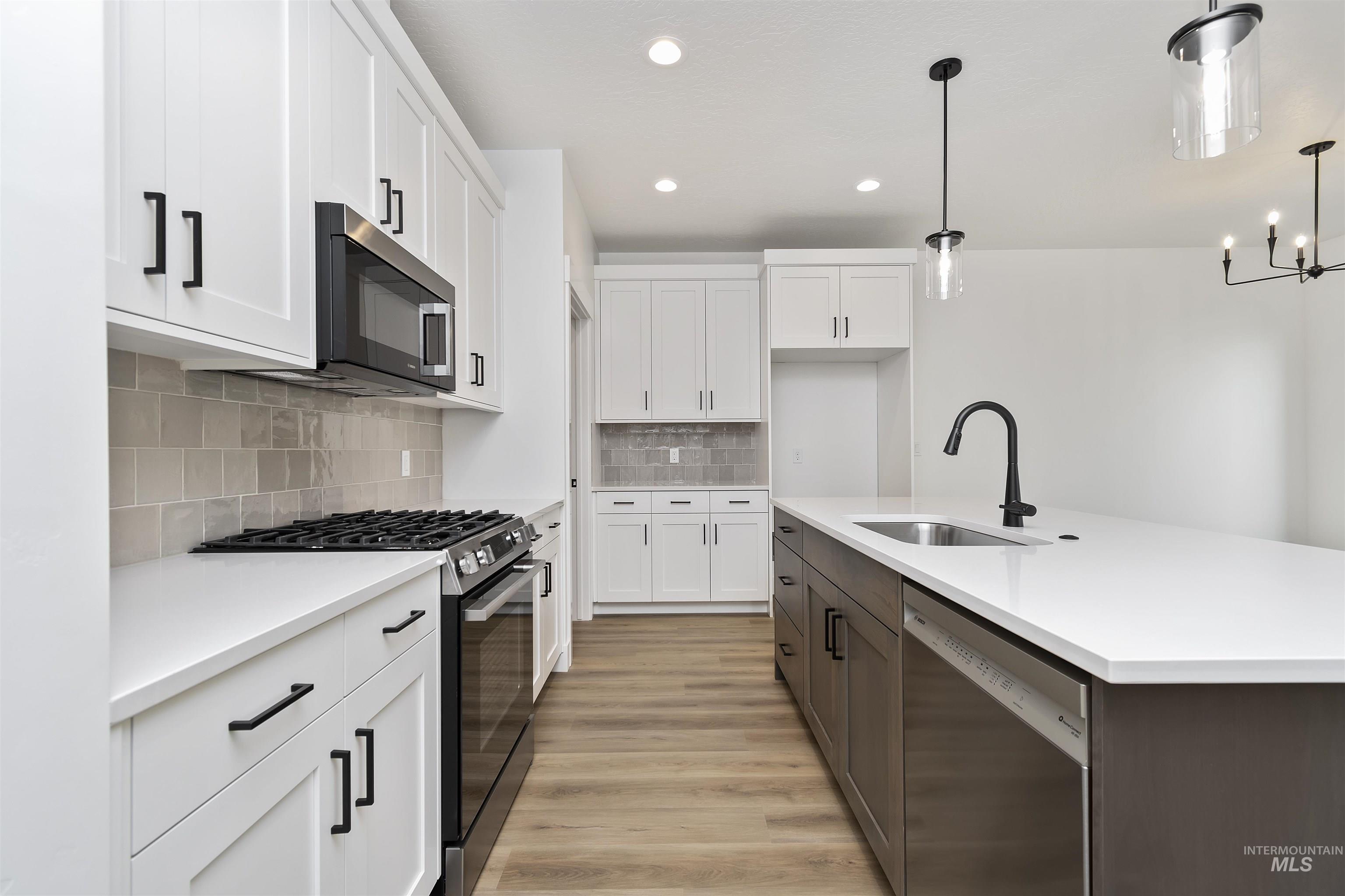 764 South Calhoun Lane Star, ID 83669 - Photo 14 of 48 Kitchen with appliances with stainless steel finishes, white cabinets, light wood finished floors, hanging light fixtures, and an island with sink