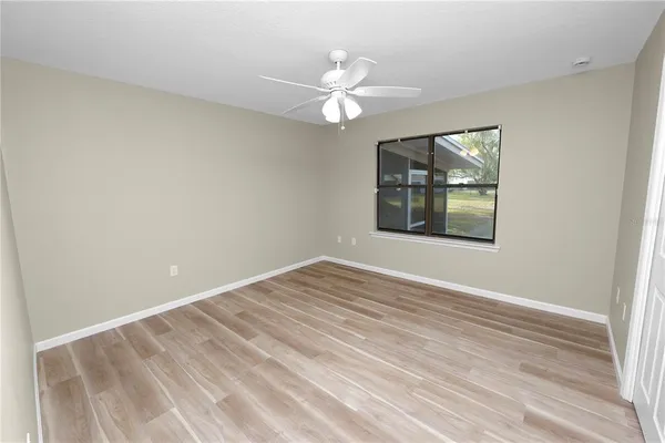 an empty room with wooden floor fan and windows