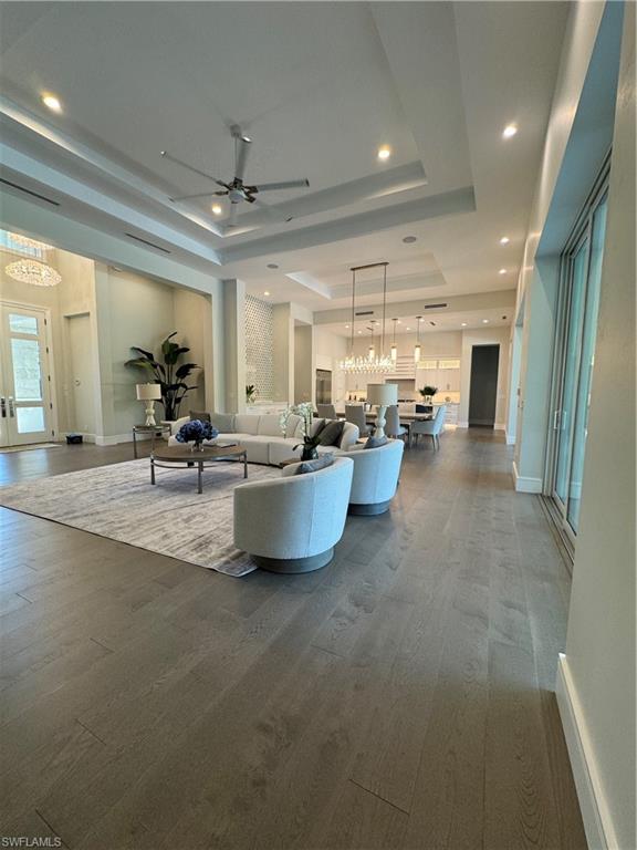 569 Neapolitan Way Naples, FL 34103 - Photo 8 of 50 Unfurnished living room featuring dark wood finished floors, a tray ceiling, and ceiling fan with notable chandelier