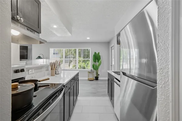 a kitchen with stainless steel appliances granite countertop a refrigerator a sink dishwasher a stove and a dining table with wooden floor