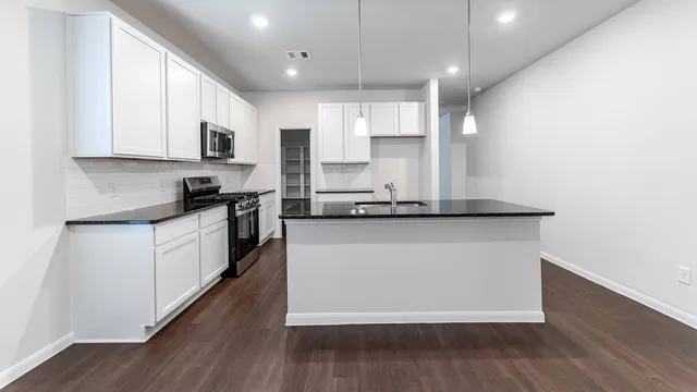 a large kitchen with stainless steel appliances granite countertop a stove a sink and white cabinets