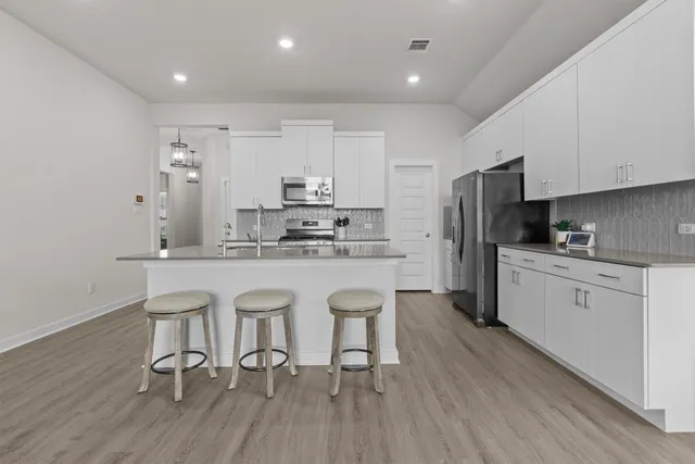 a kitchen with stainless steel appliances a refrigerator a stove a sink dishwasher and white cabinets with wooden floor