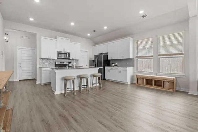 a kitchen with stainless steel appliances a stove top oven a sink a refrigerator white cabinets and wooden floor