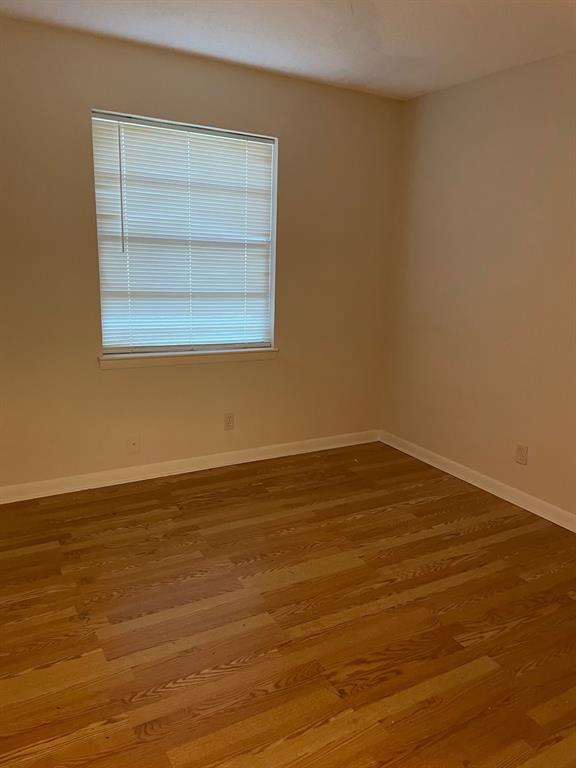 102 Roma Drive Garland, TX 75041 - Photo 8 of 9 Room featuring wood-finish flooring, neutral wall paint, white baseboards, and a window with horizontal blinds