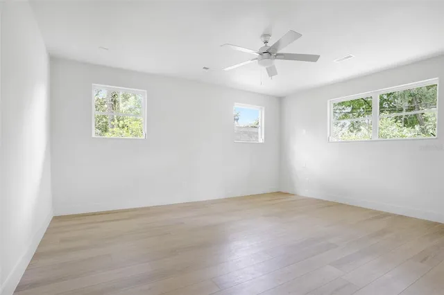 an empty room with wooden floor chandelier fan and windows