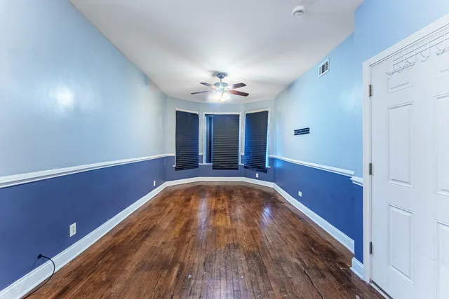 a view of an empty room with chandelier fan and wooden floor