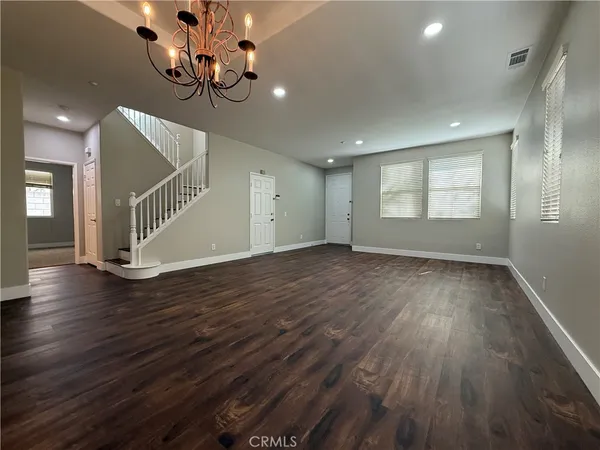 an empty room with wooden floor chandelier and windows