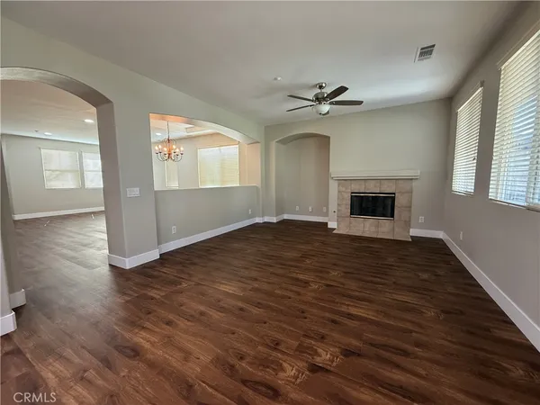 an empty room with wooden floor chandelier fan and windows