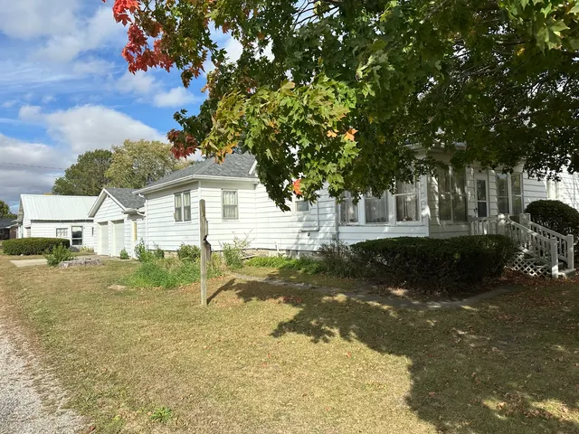 a view of a white house next to a yard with big trees