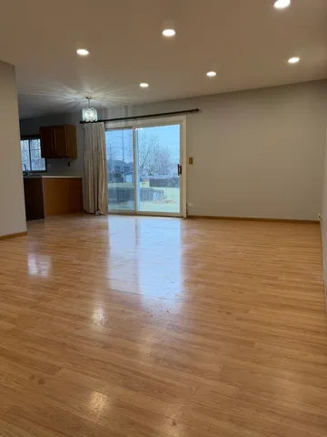 a view of an empty room with wooden floor and a kitchen