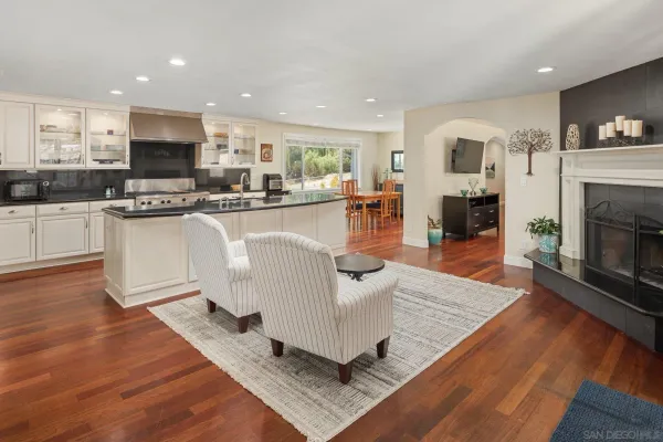 a living room with stainless steel appliances furniture a fireplace a flat screen tv and view kitchen