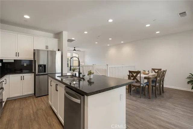 a kitchen with stainless steel appliances granite countertop a stove a refrigerator a kitchen island a dining table and chairs with wooden floor