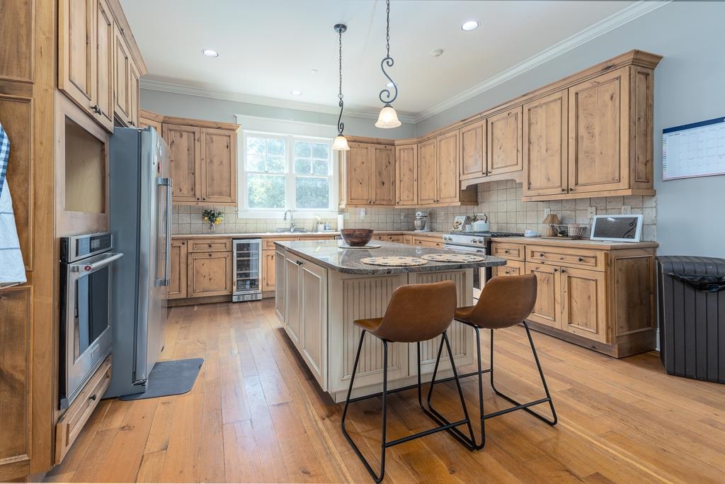 1915 Teague Store Road Somerville, TN 38068 - Photo 18 of 38 Spacious kitchen featuring extensive wood cabinetry, wood-finish flooring, a central island with a stone countertop, stainless steel appliances, and a built-in wine refrigerator