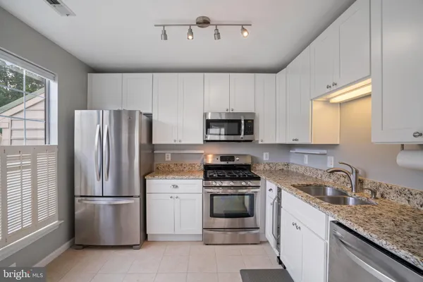 a kitchen with stainless steel appliances granite countertop a sink stove refrigerator and white cabinets with wooden floor