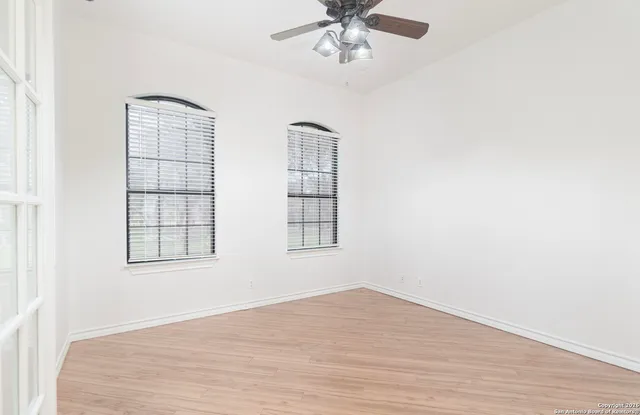 an empty room with wooden floor fan and windows