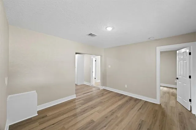 a view of an empty room with wooden floor and a bathroom