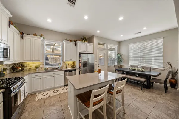 a kitchen with stainless steel appliances granite countertop a stove a sink dishwasher a refrigerator and white cabinets with wooden floor