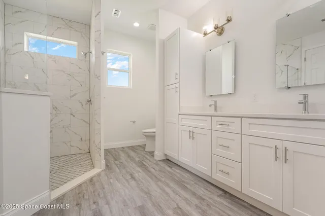 a spacious bathroom with a double vanity sink a large mirror a toilet and a shower