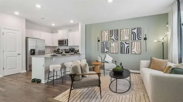 a living room with white couches and kitchen view with wooden floor