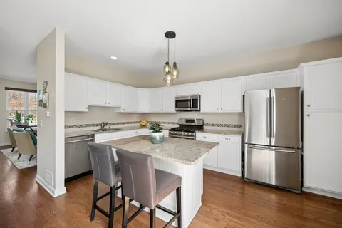 a kitchen with stainless steel appliances granite countertop a refrigerator a stove a sink dishwasher a dining table and chairs with wooden floor