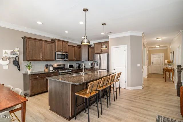 a kitchen with stainless steel appliances granite countertop a kitchen island a stove a refrigerator a sink a dining table and chairs with wooden floor