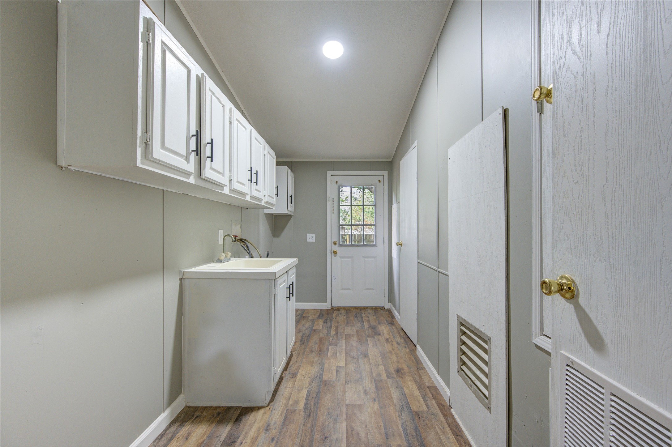 30226 Davis Street Magnolia, TX 77355 - Photo 25 of 50 This photo shows a functional utility room with white cabinets, a sink, and wood-style flooring. It has a door leading outside, providing natural light and easy access.