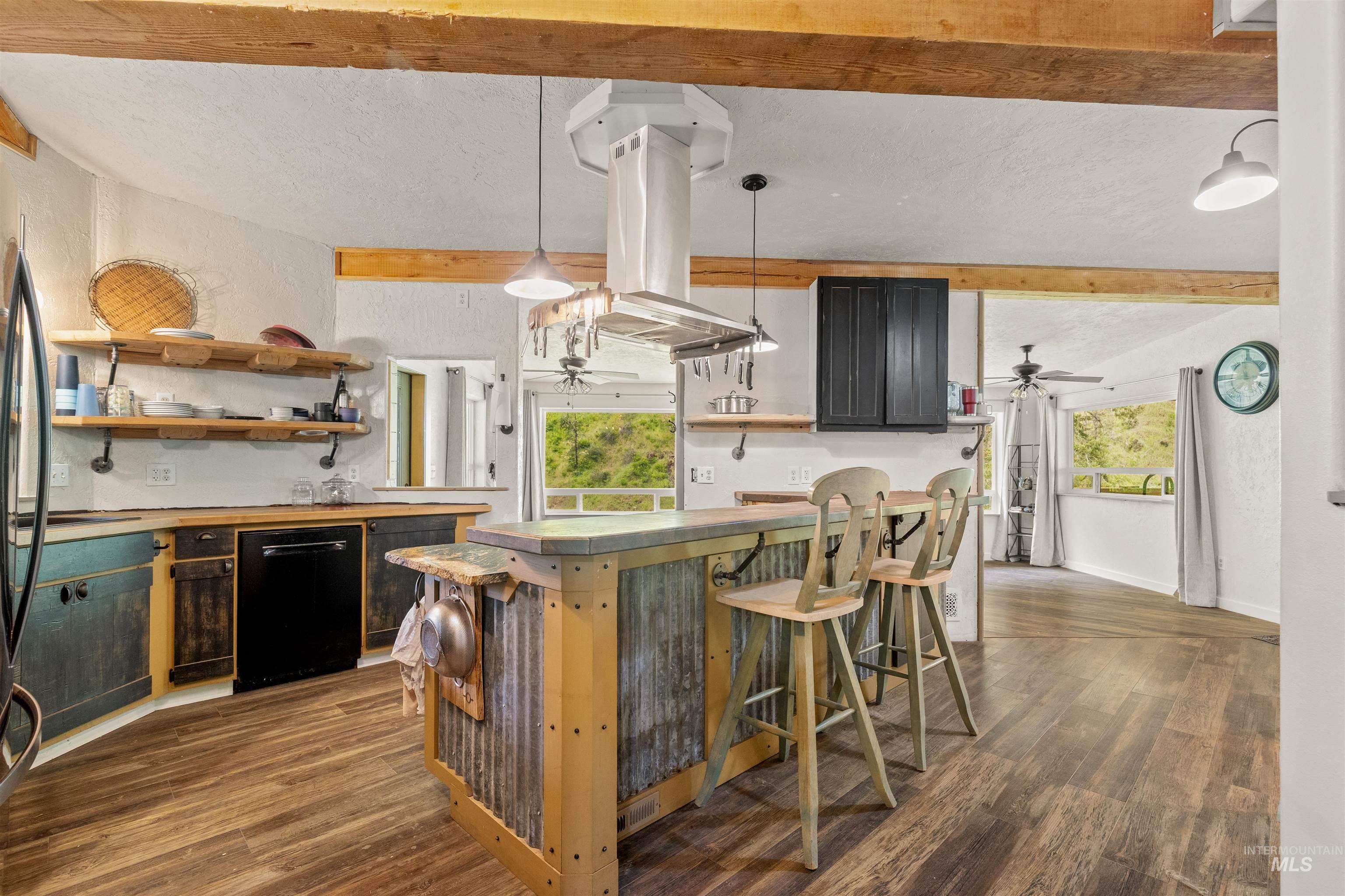 1314 Cedar Ridge Road Kendrick, ID 83537 - Photo 18 of 50 Rustic-industrial kitchen featuring exposed wood beams, wood-finish flooring, a corrugated metal island with seating, open shelving, and a stainless steel range hood