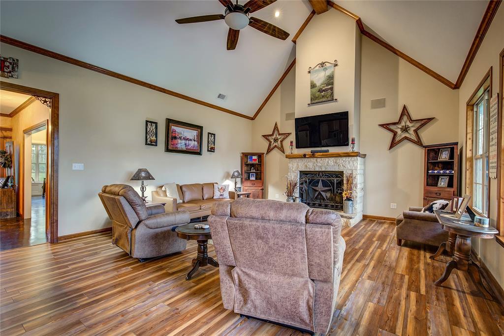811 County Road 4250 Point, TX 75472 - Photo 10 of 37 Living room featuring soaring ceilings, a stone wood-burning fireplace, newly finished wood flooring, and large windows that fill the space with natural light and beautiful countryside views.