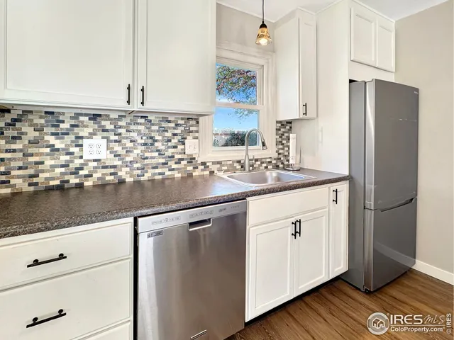 a kitchen with stainless steel appliances granite countertop a sink a refrigerator and white cabinets