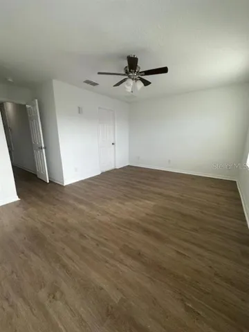 an empty room with wooden floor fan and windows