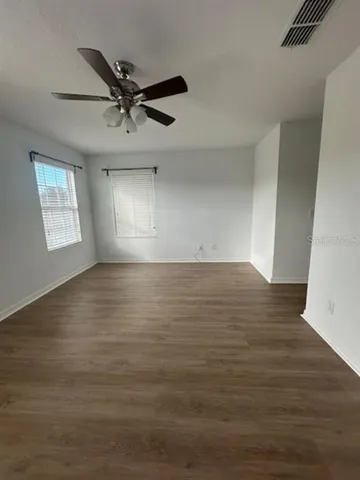 an empty room with wooden floor fan and windows