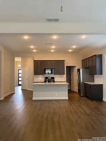 a large kitchen with stainless steel appliances a large counter top a sink dishwasher a refrigerator and a stove with wooden floor