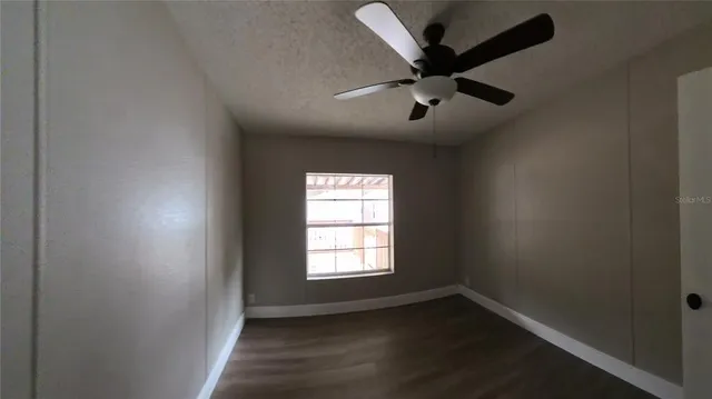 an empty room with wooden floor ceiling fan and windows