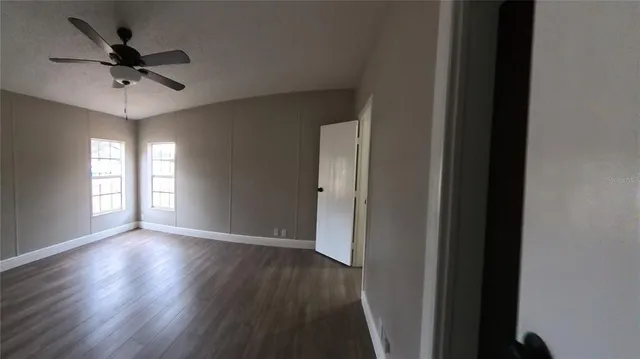 an empty room with wooden floor fan and windows