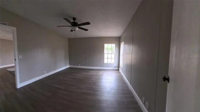 an empty room with wooden floor fan and windows