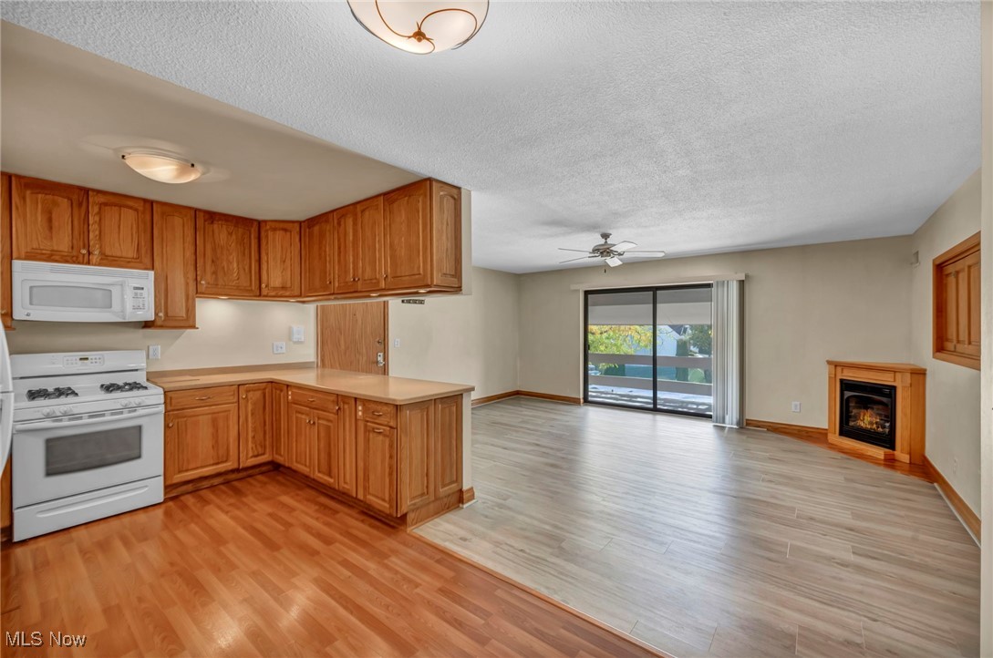 1263 Lost Nation Road, Unit 5 Willoughby, OH 44094 - Photo 12 of 26 Kitchen featuring white appliances, light countertops, a glass covered fireplace, light wood-style flooring, and a textured ceiling