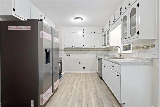 a kitchen with granite countertop a refrigerator a sink and white cabinets
