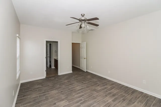 a view of an empty room with wooden floor and a ceiling fan