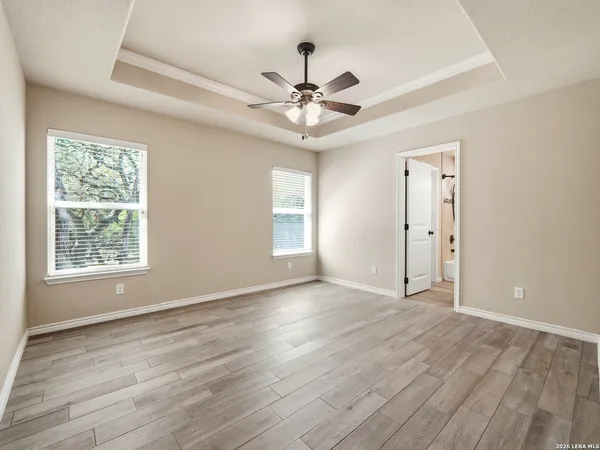 an empty room with wooden floor chandelier fan and windows