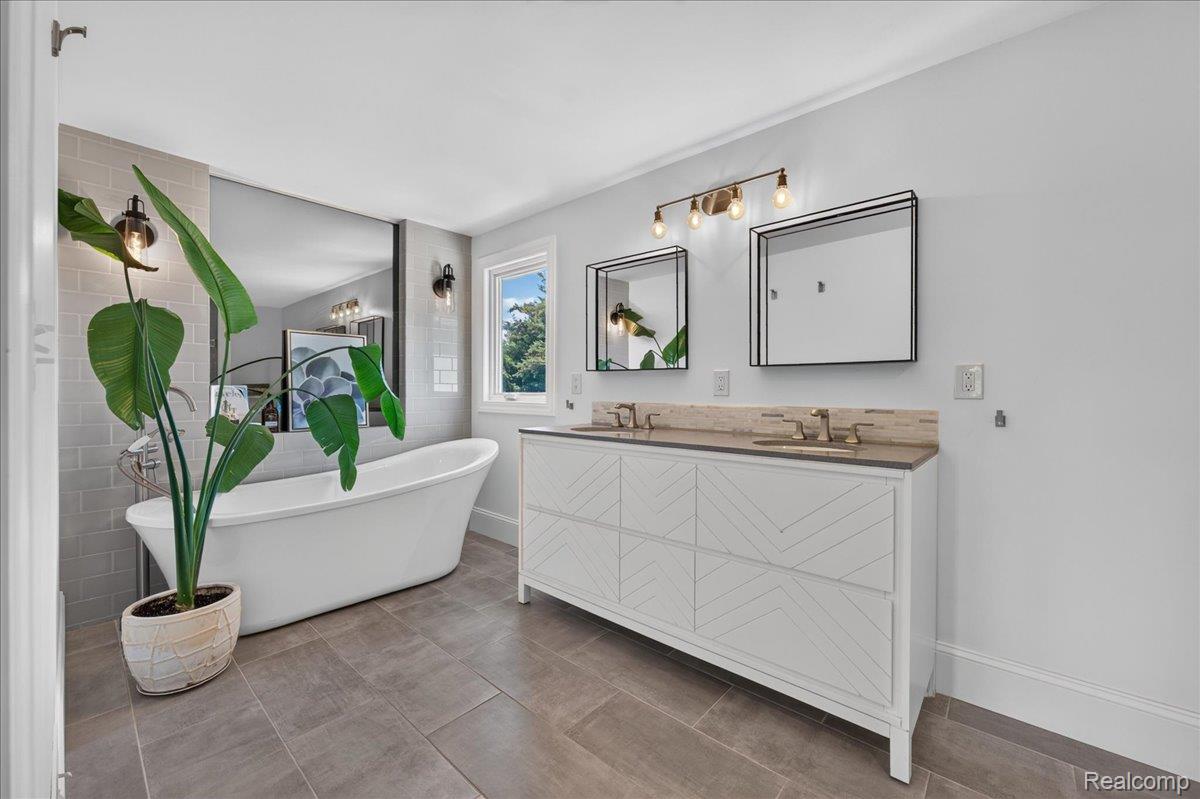 7330 West Gates Street Romeo, MI 48065 - Photo 34 of 73 Freestanding soaking tub, dual vanity with patterned cabinetry, rectangular framed mirrors, and wall-mounted sconces